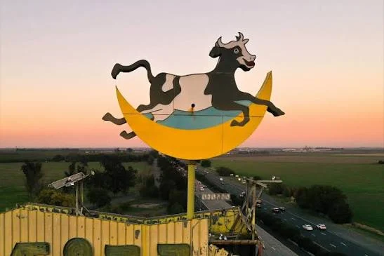 The original cow leaping over a golden crescent moon atop the Milk Farm sign